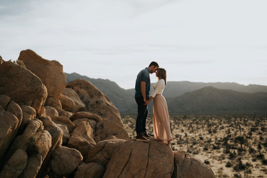 man and woman posing on top of boulders, couple with forehead touching, Moody Couples Session at Joshua Tree