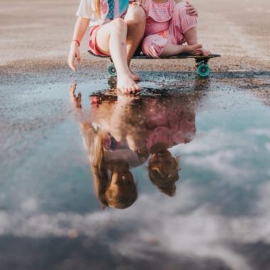 Two girls sitting on skateboard looking at reflection, puddle reflection image, Photos by Lindsey Daily Fan Favorite