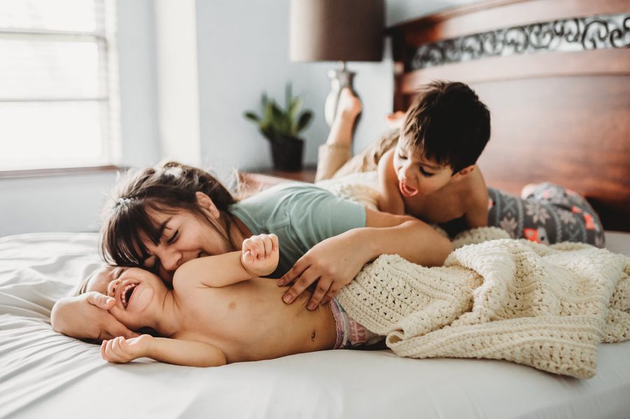 mom snuggling with kids on bed, tickle fight