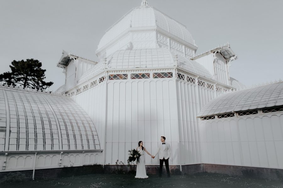 Couple holding hands in front of building, Portrait outside of Conservatory of Flowers, Edgy Styled Wedding Portraits in San Francisco
