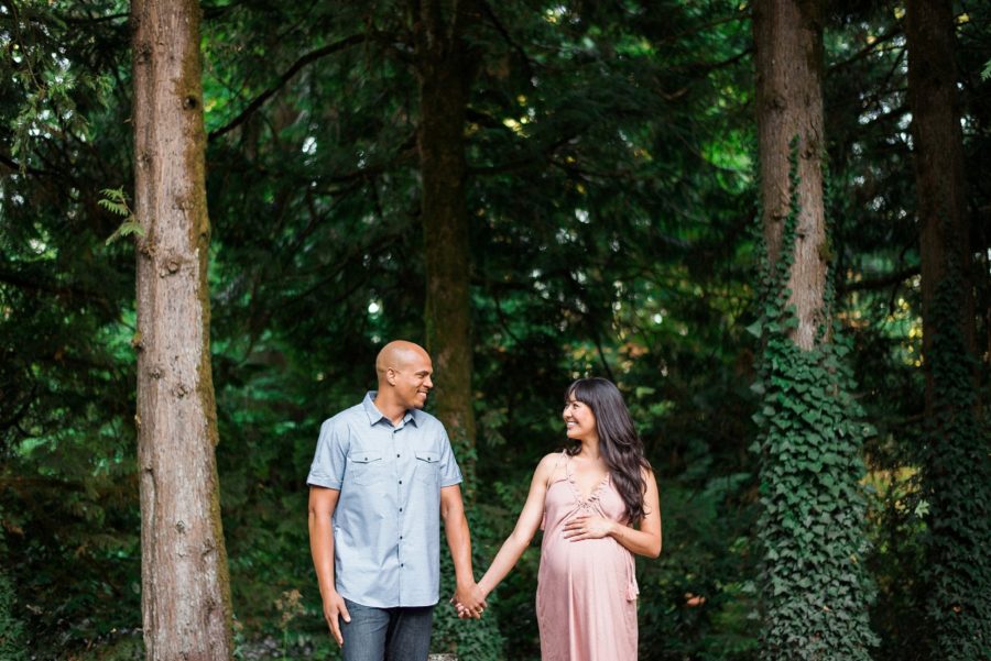 Pregnant woman holding hands with man and smiling in woods, Pittock Mansion Gardens Maternity Session