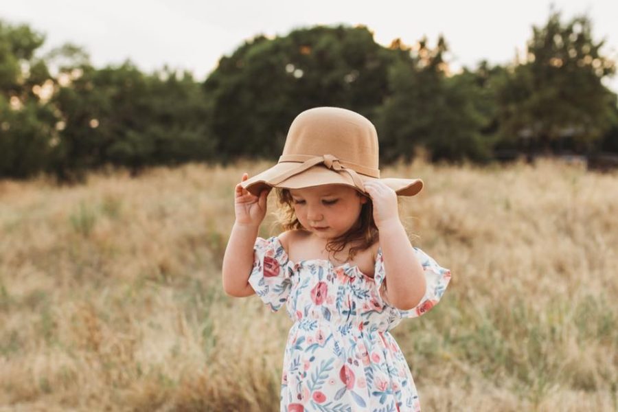 Little girl standing in field touching hat wearing floral dress, Beyond the Wanderlust Daily Fan Favorite