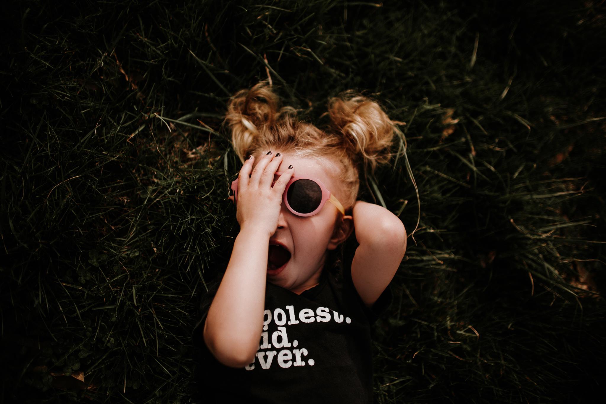 spring pictures of kids, little girl wearing sunglasses laying in grass, funny kid shirts, little girl fashion, sassy little girl