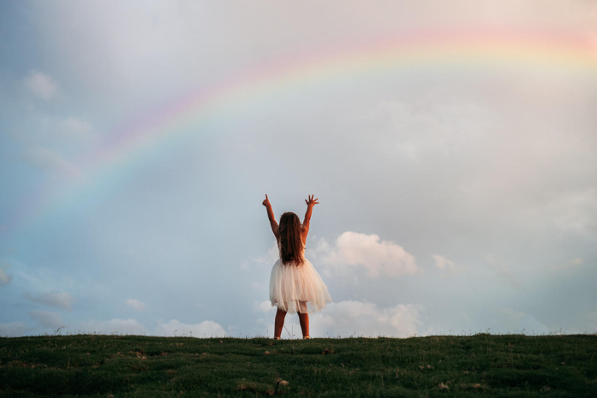little girl standing in front of colorful sky with rainbow